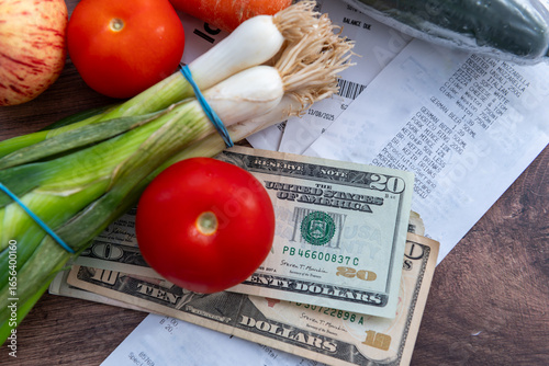 A US cost of living concept with a pile of US Dollar bills, grocery receipts and some fruit and vegetable groceries on a table.