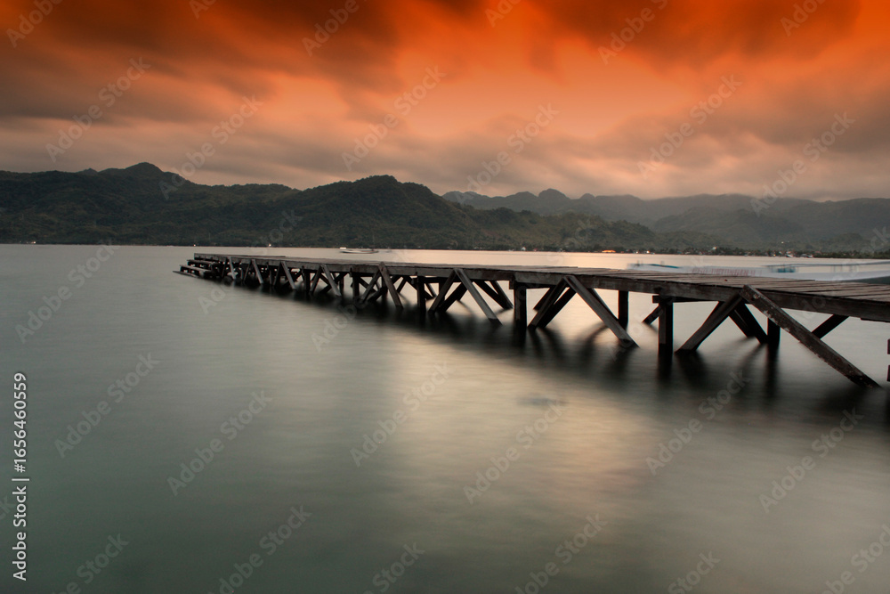 Obraz premium Serene pier extends into calm water at dramatic sunset