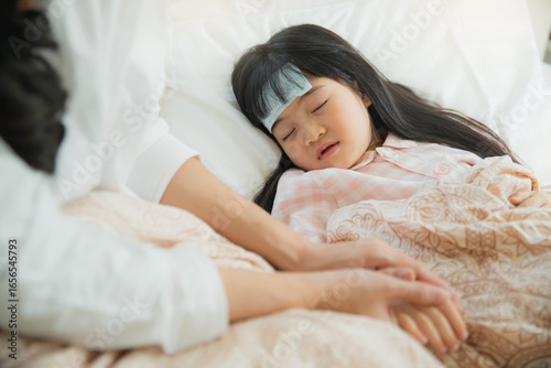 Sick little child with temperature in bed. Hand of mother on his forehead. photo of caring mother holding head on sick daughter forehead.