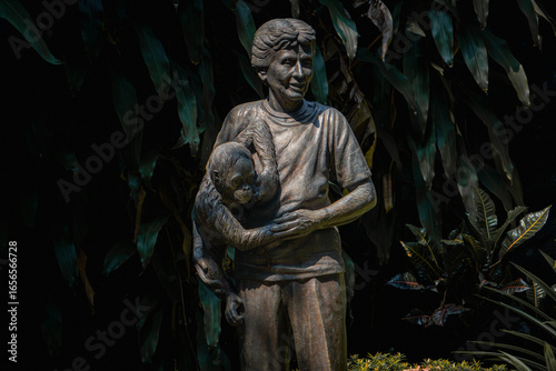 Tableau sur toile Schmutzer Primate Center, Jakarta - June 12, 2025: The statue of Pauline Antoinette Adeline Schmutzer holding a gorilla cub, displayed outdoors with surrounding plants creating natural atmosphere