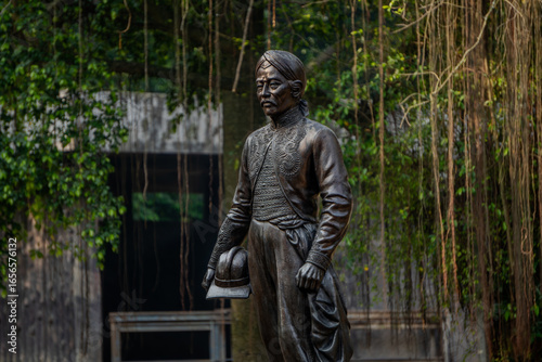 Obraz na plátně Ragunan Zoo, Jakarta - June 12, 2025: Detailed bronze statue of the historical figure Raden Saleh in traditional attire, holding a book, with trees and a building in the background