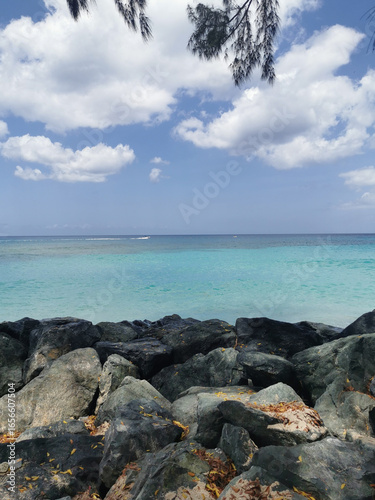 Rugged coastal rocks meeting the vibrant turquoise waters of the Caribbean Sea under a bright blue, cloudy sky