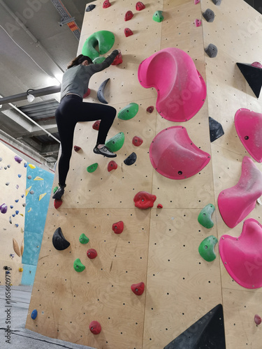 Female climber focused on ascending a colorful indoor bouldering wall, reaching for a hold. Dynamic and active lifestyle.

