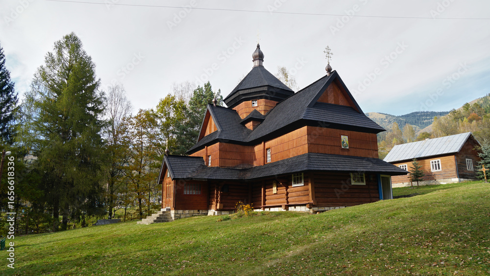 Fototapeta premium A historic wooden Orthodox church stands on a green hill in the Carpathian Mountains, embodying traditional Ukrainian folk architecture and spiritual heritage.