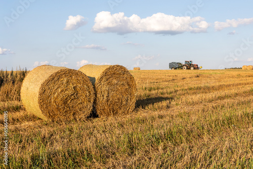 Round hay bales in field with baler wrapper machine working in background