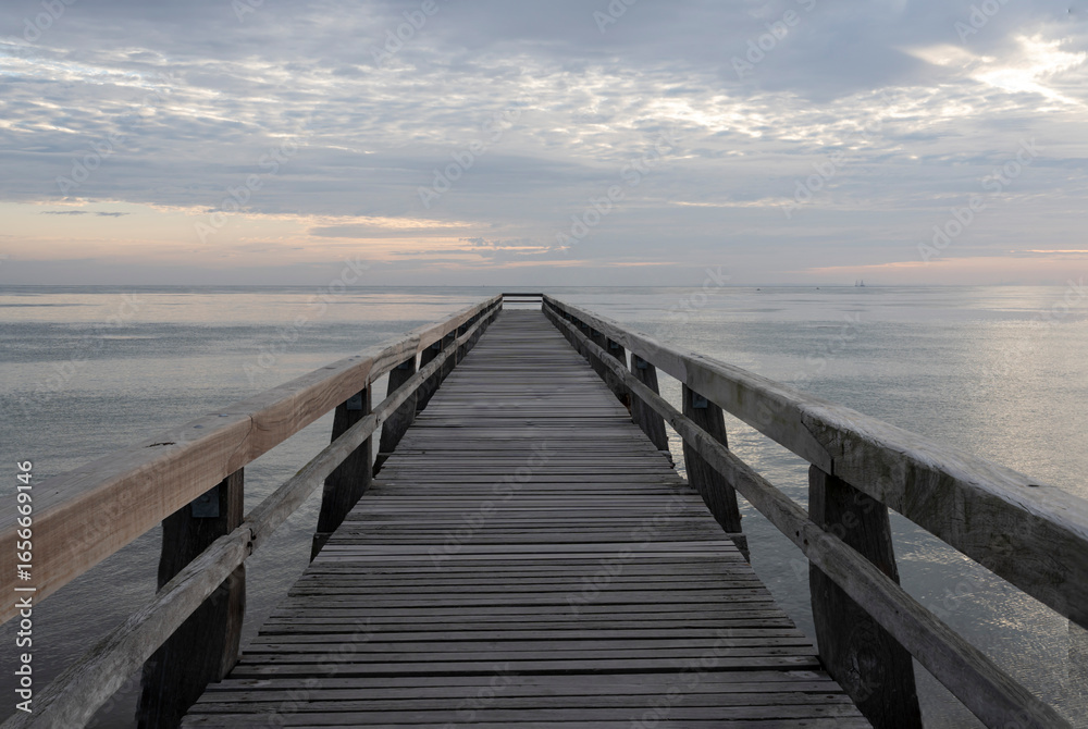 Obraz premium Luc-Sur-Mer, France - 08 07 2025: View of the wooden pier in front of the sea named Fisherman's Pier at sunrise and Le Havre far away