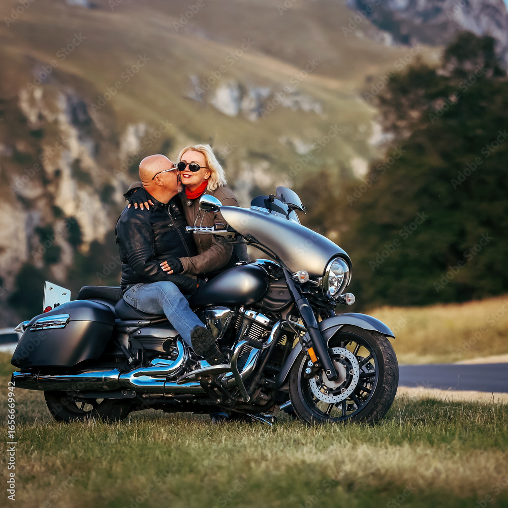 Obraz premium Romantic couple enjoying a tender moment on a cruiser motorcycle in the mountains at sunset, symbolizing love, freedom, and adventure travel lifestyle