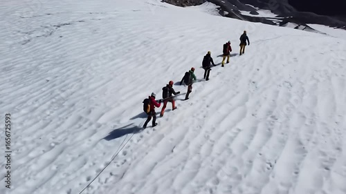 A line of hikers traverse a snowy mountain landscape under a partially cloudy sky