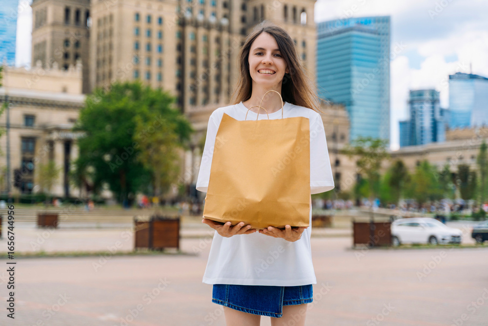 Fototapeta premium Happy woman holding kraft paper shopping bag outdoors in city