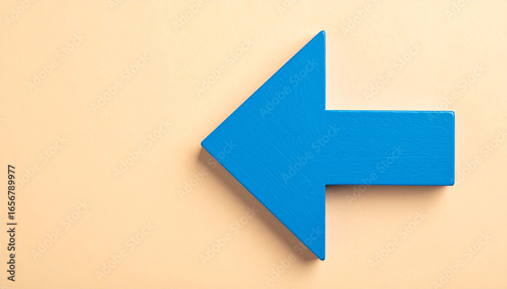 Fototapeta premium Blue wooden arrow pointing left on beige backdrop. Return, backtracking, business concept.