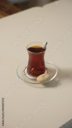 A traditional glass of tea served alongside a delicate cookie on a saucer, reflecting a serene moment conducive to relaxation and gentle conversation over a warm drink, fa01