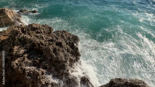 Witness the vibrant turquoise waves dramatically crashing onto stones. An awe-inspiring coastal visual ideal for travel and nature documentaries.