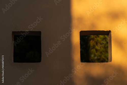 Minimalist wall with two square windows casting shadows in warm evening sunlight in Crete, Greece