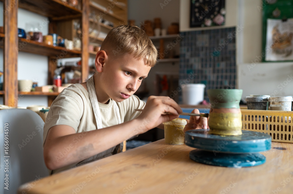 Fototapeta premium Focused boy painting ceramic cup at home pottery studio