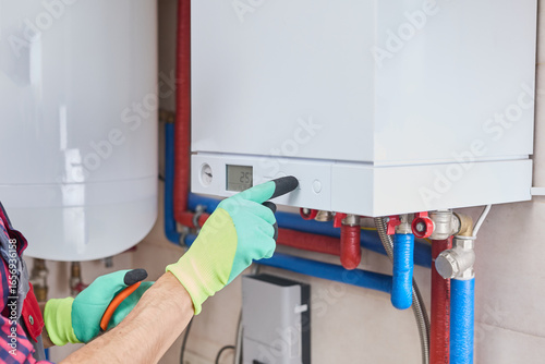 Plumber adjusting the temperature on a central heating boiler's control panel, ensuring optimal performance and energy efficiency in a home