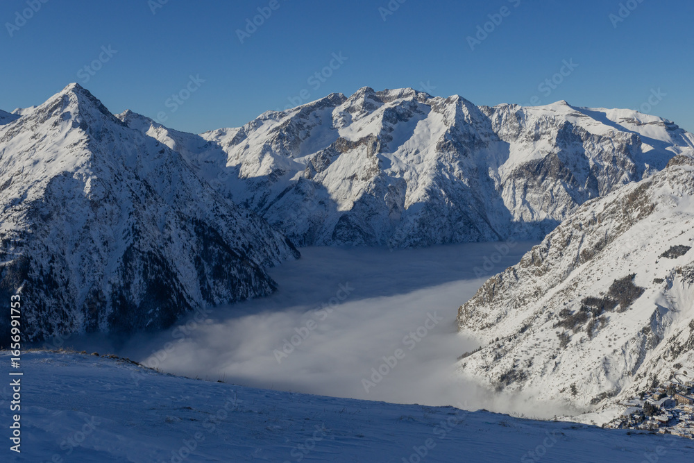 Naklejka premium Snowy mountains rise above a blanket of cloud that cover valley