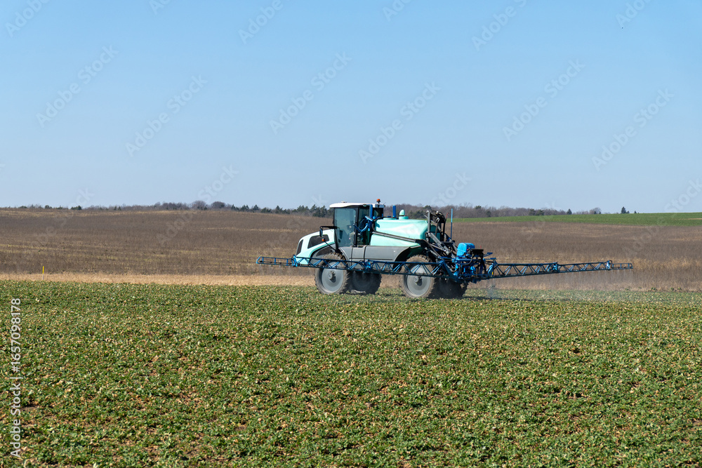 Fototapeta premium Blue wheel tractor spraying liquid fertilizer on a field during springtime.