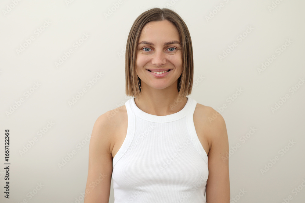 Portrait of young smiling caucasian european attractive woman 30s with straight-shoulder length brown hair in white tank top looking at camera isolated on light background. People lifestyle concept. Portrait of young smiling caucasian european attractive woman 30s with straight-shoulder length brown hair in white tank top looking at camera isolated on light background. People lifestyle concept.