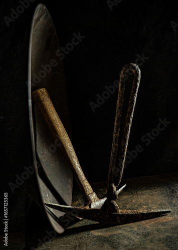 Low key image highlights mining tools including gold pan & hand picks for digging. Handles are wood & hand wrought iron. Gold pan rim is highlighted.