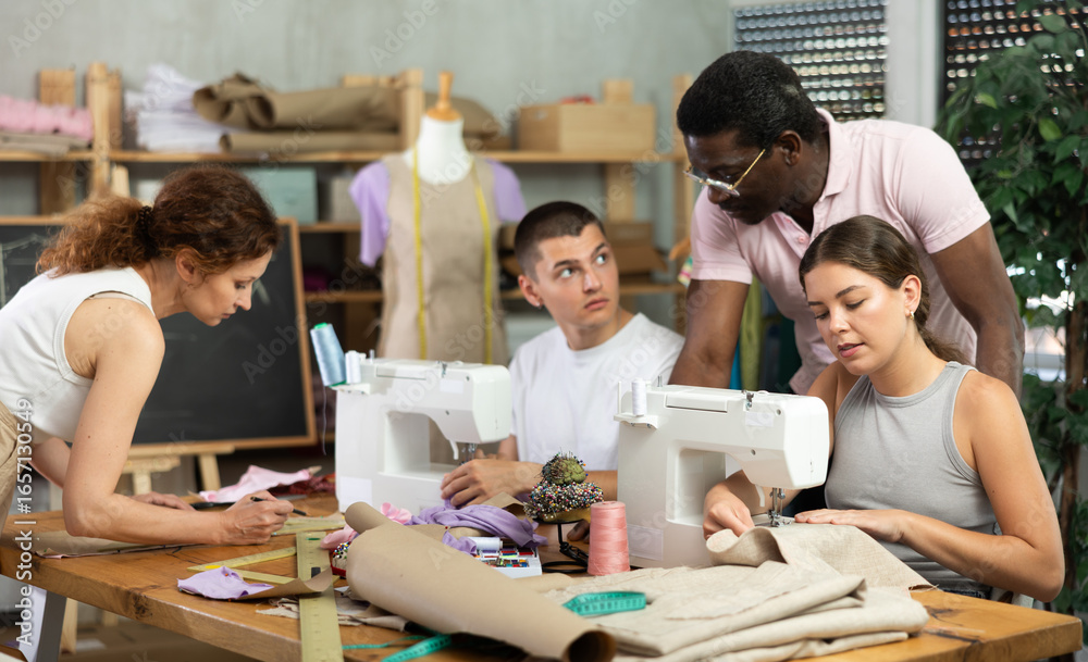 Obraz premium During lesson, African male teacher helps student sew, while others sew and work with paper, draw dress pattern. Interest group, activities, hobbies, vocational training..