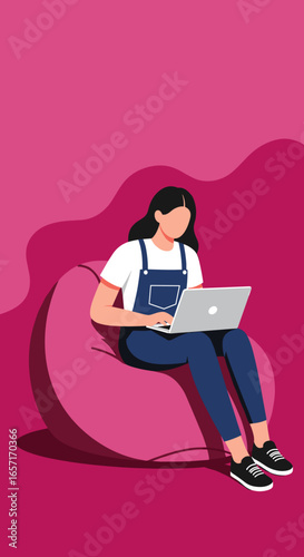 Relaxed woman in overalls works comfortably on her laptop from a pink bean bag chair. Ideal for concepts of remote work, freelancing, and flexible lifestyle.