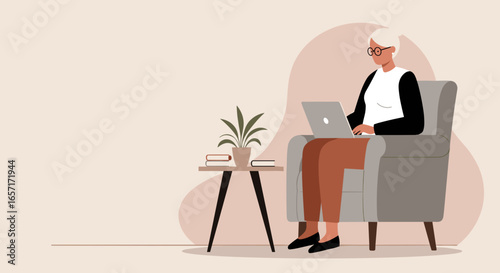 Elderly woman comfortably working or learning from home on her laptop in an armchair, showcasing modern senior life and digital engagement.
