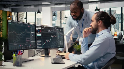 Prop firm staff members communicate at PC desk to ensure smooth trading operations. Team of traders in office doing brainstorming, discussing market trends and portfolio positions, camera A