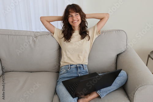 Obraz na plátně Happy beautiful curly brunette sitting on the sofa with arms crossed behind head