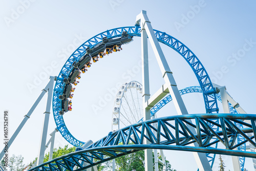 Fototapeta Naklejka Na Ścianę i Meble -  Roller coaster Ride against blue sky. Roller coaster in the amusement park. Cheerful entertainments in park of attractions
