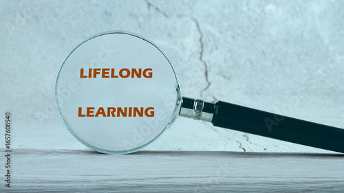 A magnifying glass highlights the phrase lifelong learning against a textured background, emphasizing continuous education in business