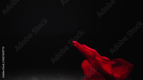 Light transparent red fabric floats in the air. Slow motion fall of red cloth in the dark