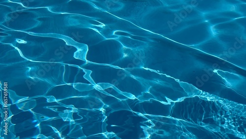 Horizontal photo of deep blue rippling water in swimming pool with sun reflection and magic feel.