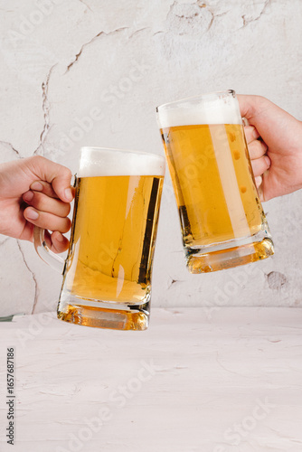Two Hands Toasting with Beer Mugs Against Marble Background