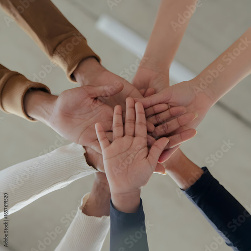This image shows several hands of different people stacked together in a gesture of unity and teamwork. The hands belong to both adults and children, symbolizing togetherness, support.
