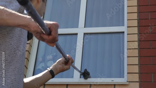 Man washing tall house window with cleaning tool