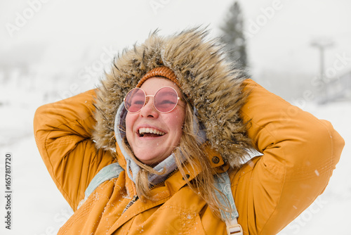 Happy woman in fur jacket enjoying snowfall at vacation