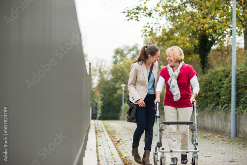 Adult granddaughter assisting her grandmother walking with wheeled walker