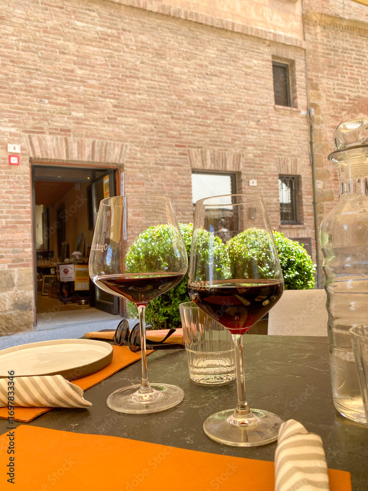 Naklejka premium Wine glasses resting on rustic table near stone building in Montepulciano, Tuscany