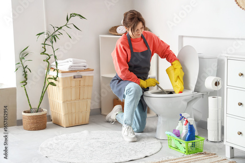 Young woman cleaning toilet...