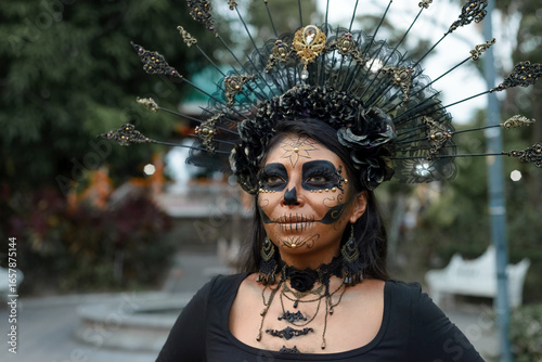 A woman adorned in elaborate Day of the Dead makeup and a stunning black and gold headdress.