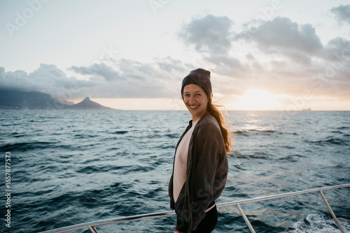 South Africa, young woman with woolly hat smiling during boat trip at sunset