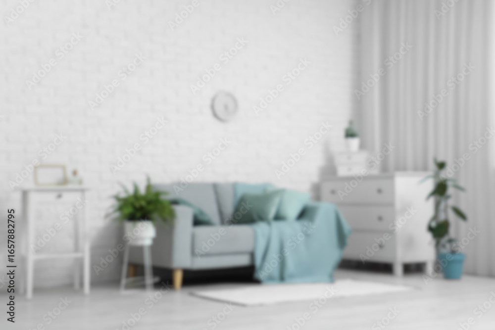 Fototapeta premium Grey sofa, houseplants, chest of drawers and clock on white brick wall in stylish living room, blurred view