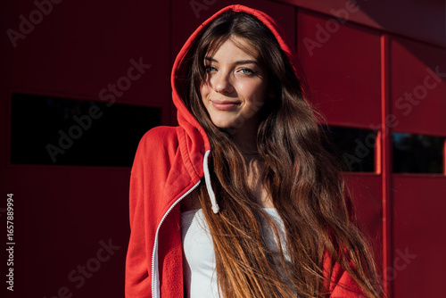 Smiling teenage girl wearing red hooded jacket on sunny day
