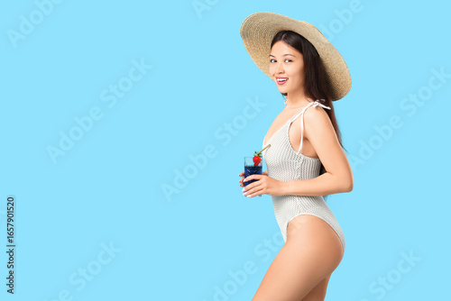 Beautiful young Asian woman in swimsuit and wicker hat with glass of cocktail...
