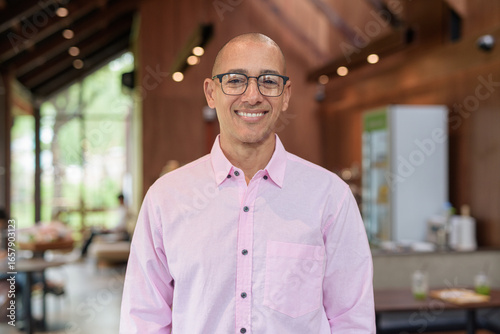Bald Hispanic man wearing pink casual business shirt and eyeglasses in coffee shop cafe restaurant