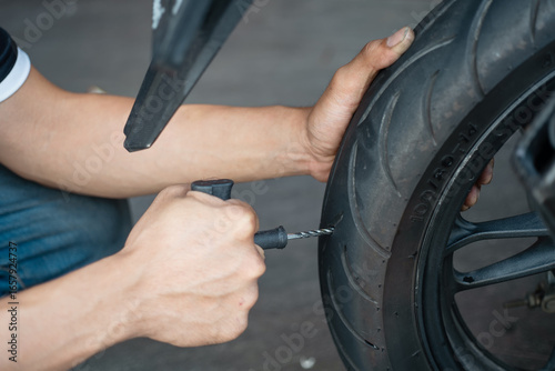 Rider use a tire plug kit or reamer plugger tool and trying to fix a hole in tire's sidewall ,Repair a motorcycle flat tire in the garage. motorcycle maintenance and repair concept