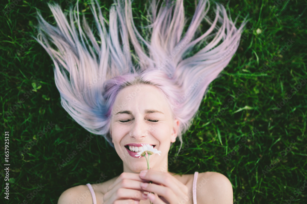 Portrait of laughing woman lying on grass with eyes closed holding daisies Portrait of laughing woman lying on grass with eyes closed holding daisies