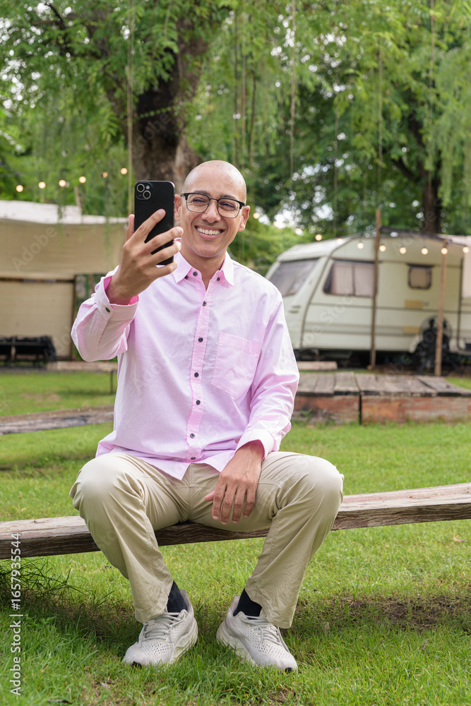 Obraz premium Full length portrait of bald Hispanic man outdoors using phone in park