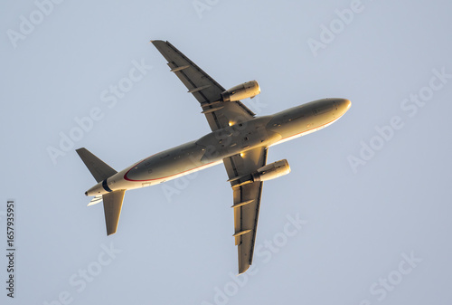 Low angle view capturing passenger airplane soaring against clear blue sky, revealing aircraft underside details and wing configuration