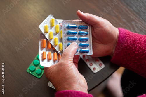 Elderly woman holds medications in her hands. A pensioner at home examines several blister packs, capturing everyday medical dependency in old age